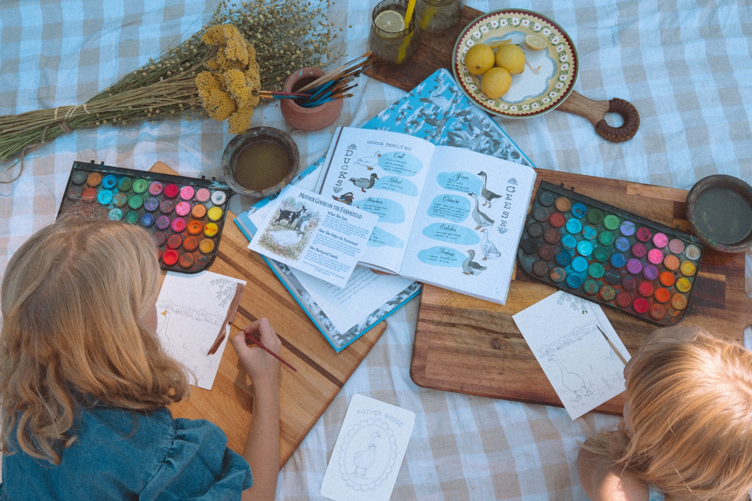 Children painting Mother Goose watercolor pages at an outdoor farm table